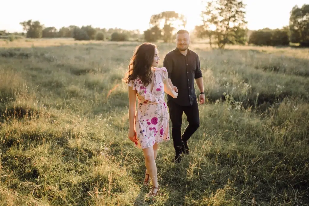 Un couple se tenant la main dans une prairie au soleil couchant